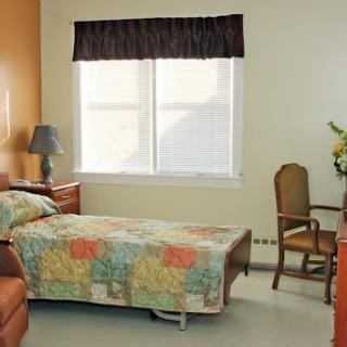 A cozy and well-lit bedroom featuring a bed with a colorful quilt, a desk, and a window allowing natural light.