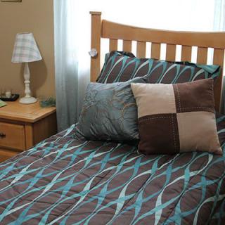 A neatly made bed with patterned bedding and decorative pillows alongside a wooden nightstand and lamp.