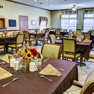 A well-organized dining room with neatly arranged tables and chairs, featuring floral centerpieces and napkins.