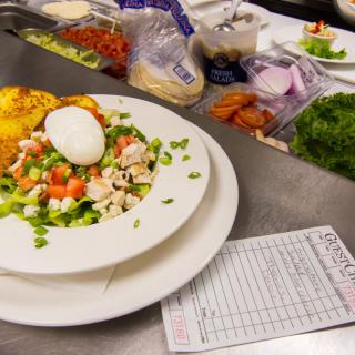 A fresh salad topped with a poached egg, ready for serving in a busy kitchen.