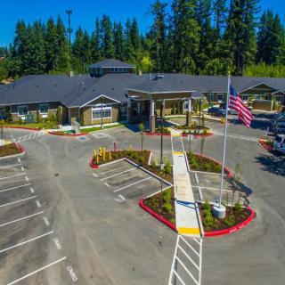 Aerial view of a modern building with a parking lot and landscaped entrance surrounded by trees.