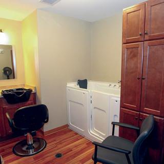 A multifunctional room featuring washing machines and a salon station with a sink, mirror, and chairs.