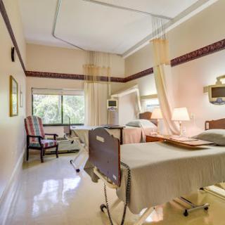 A well-designed hospital patient room featuring two beds, a sitting area, and natural light from the window.