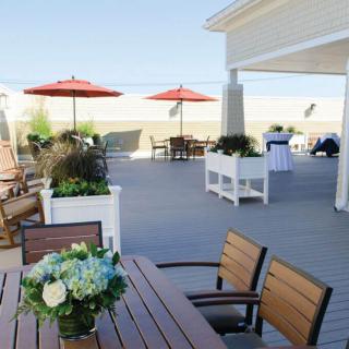 A spacious outdoor patio with tables, chairs, and red umbrellas, adorned with a flower arrangement on the table.