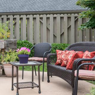 A cozy patio setup with chairs, a table, and plants against a wooden fence.