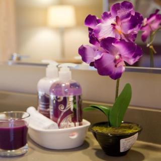 A bathroom counter with a purple orchid, soap dispensers, and a candle.