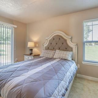 A cozy bedroom with a large bed, nightstand, and windows letting in natural light.