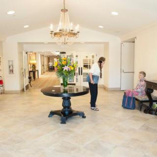 A spacious lobby with a chandelier, flowers on a round table, and two people interacting in the reception area.