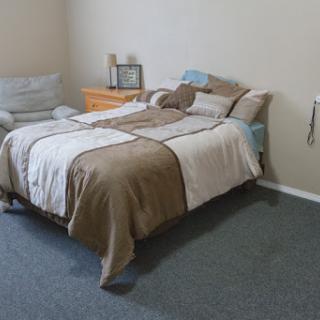 A cozy bedroom featuring a neatly made bed, a nightstand with decorative items, and a comfortable chair.