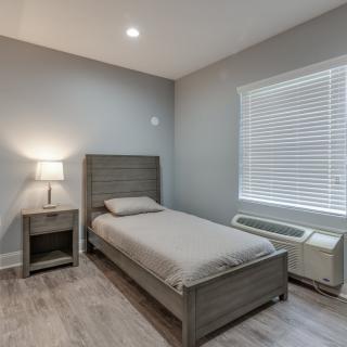A minimalist bedroom with a single bed, nightstand, and lamp.