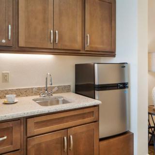 A compact kitchen area with wooden cabinets, a small sink, and a stainless steel fridge.
