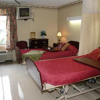 A hospital room featuring two patient beds with red bedding, equipped with a television and essential furniture.