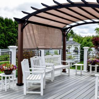 A cozy outdoor patio area with a pergola and white seating arrangements, surrounded by plants and flowers.