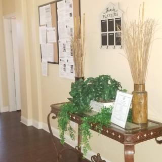 A hallway featuring a decorative table with plants and a bulletin board on the wall.