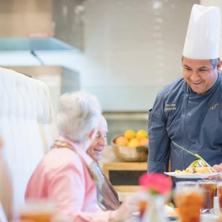 A chef serving a meal to elderly patrons in a restaurant setting.