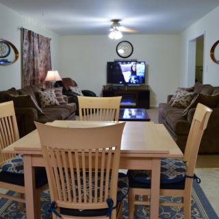 A cozy living room with a dining table and sofas facing a television, complemented by a ceiling fan.