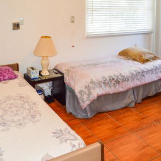 A cozy bedroom with two beds, a lamp on a side table, and wooden flooring.