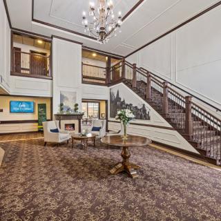 A spacious lobby with elegant interior design features a grand staircase, a chandelier, and comfortable seating.