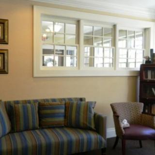 A cozy living room with a striped sofa and an armchair, featuring window panels and a bookshelf.
