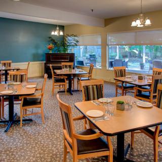 An empty dining room with wooden tables and chairs, featuring large windows and chandeliers.