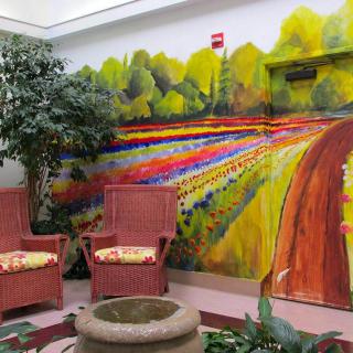 An indoor seating area featuring a vibrant mural of a scenic landscape with colorful fields and trees.