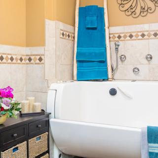 A cozy bathroom with a white bathtub, neatly folded blue towels, decorative candles, and wicker storage baskets.