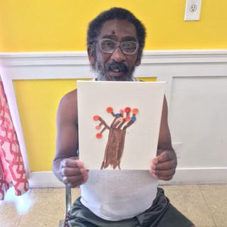 A man holding up a drawing of a tree with red leaves.