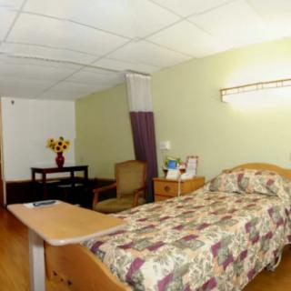 A hospital room with a single bed, chair, and small table with flowers.