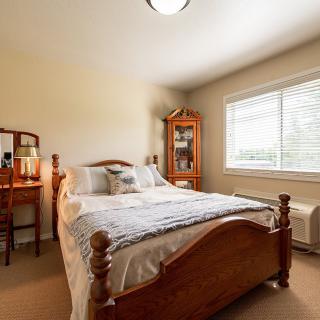 A cozy bedroom with a wooden bed frame, decorated with pillows and a quilt, bathed in natural light from the window.
