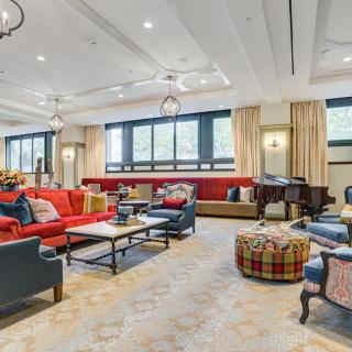Spacious and elegantly designed living room with luxurious sofas and a grand piano, featuring ample natural light from large windows.