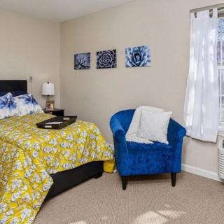 A cozy bedroom featuring a yellow floral bedspread, a vibrant blue armchair, and wall art that complements the decor.