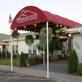 A building entrance with a red awning and decorative plants.
