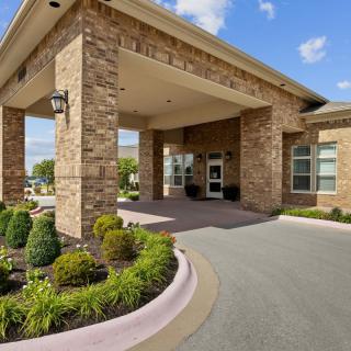 A brick building entrance with well-maintained landscaping and a driveway.