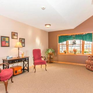 A cozy living room featuring armchairs, a desk, and a large window with green curtains.