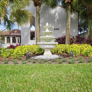 A picturesque garden scene with a tiered fountain surrounded by vibrant flowers and palm trees.