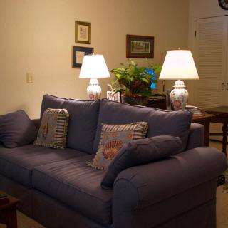 A cozy living room featuring a blue sofa with patterned cushions, flanked by two lit lamps and decorated with wall pictures and greenery.