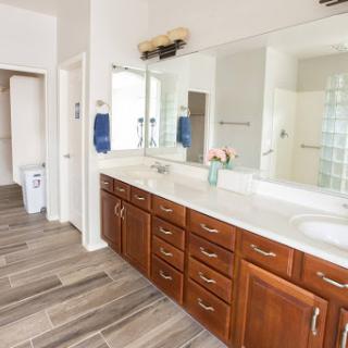 A spacious and modern bathroom featuring a double vanity with wooden cabinets, large mirrors, and stylish tile flooring.
