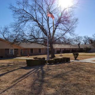A sunny day with an American flag flying in front of a building, surrounded by bare trees and grass.