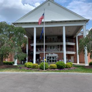 A large building with columns and an American flag flying in front, surrounded by landscaping under a cloudy sky.