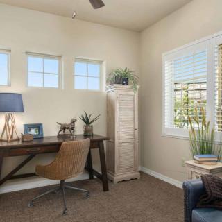 A cozy home office with a desk, chair, and natural light from the windows.