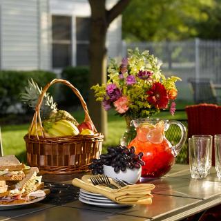 A refreshing summer picnic setup with a basket of fruits, a pitcher of juice, and fresh flowers on a table outdoors.