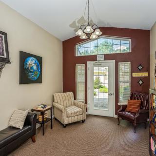 A cozy living room with comfortable chairs, a couch, and artwork on the walls. A large window lets in natural light.