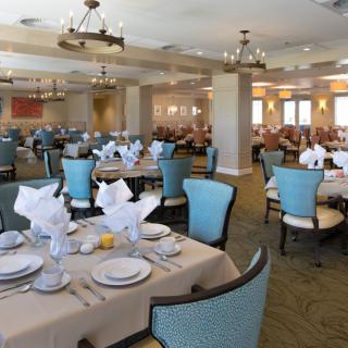 An elegantly set dining room with neatly arranged tables and chairs, featuring chandeliers and tasteful decor.
