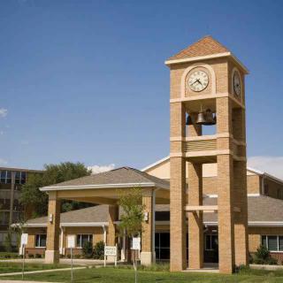 A brick clock tower standing in front of a building under a clear blue sky.