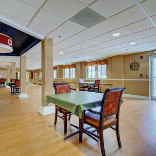 An empty dining area with neatly arranged tables and chairs, featuring a wooden floor and ample natural light from the windows.