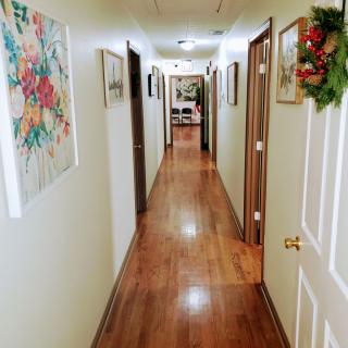 A long indoor hallway with a wooden floor, adorned with framed artwork and doors on either side.