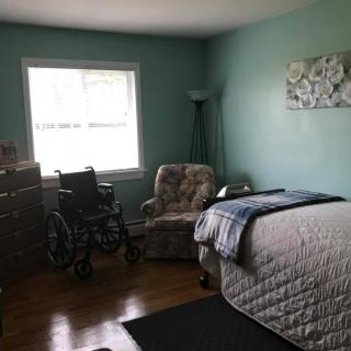 A cozy bedroom with a bed, armchair, and wheelchair by the window.