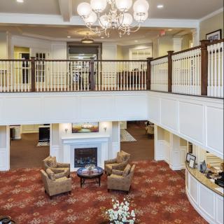 A spacious and elegantly designed lobby featuring a chandelier, armchairs, and a fireplace with a balcony overlooking the area.