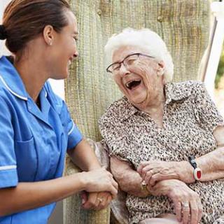 A nurse shares a joyful moment with an elderly woman outside.