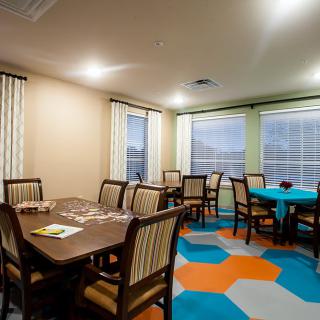 A cozy dining area with neatly arranged tables and chairs, featuring colorful carpet flooring and soft lighting.